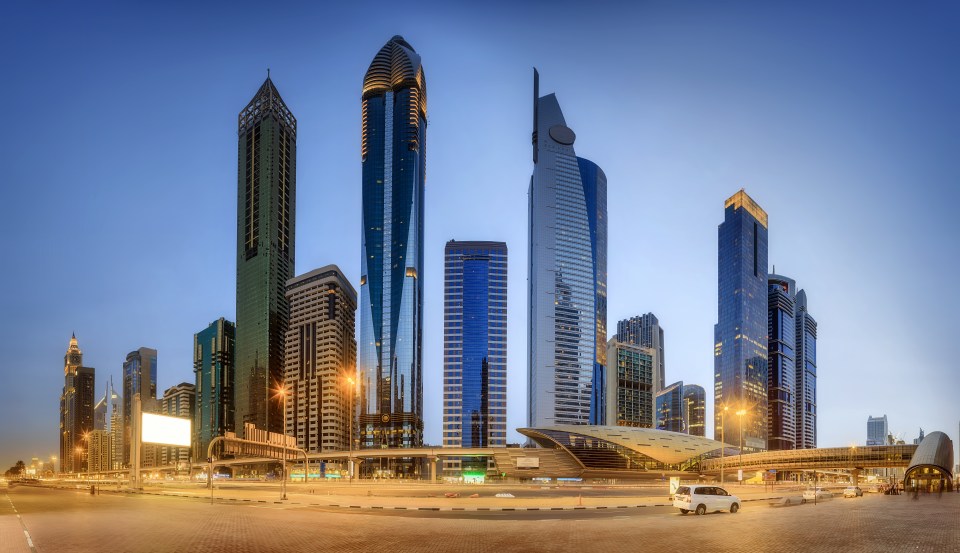 Panoramic view of Dubai's financial district at dusk, featuring skyscrapers and a metro station.