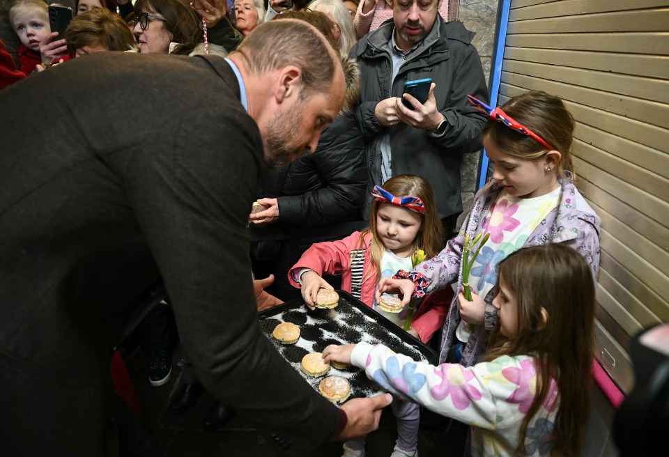 Prince William handing Welsh cakes to children at a market.