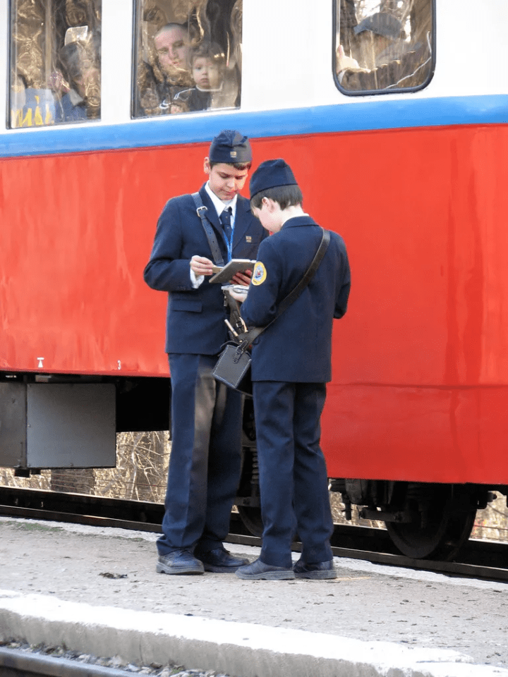 Two young men in uniform standing by a train, looking at a tablet.