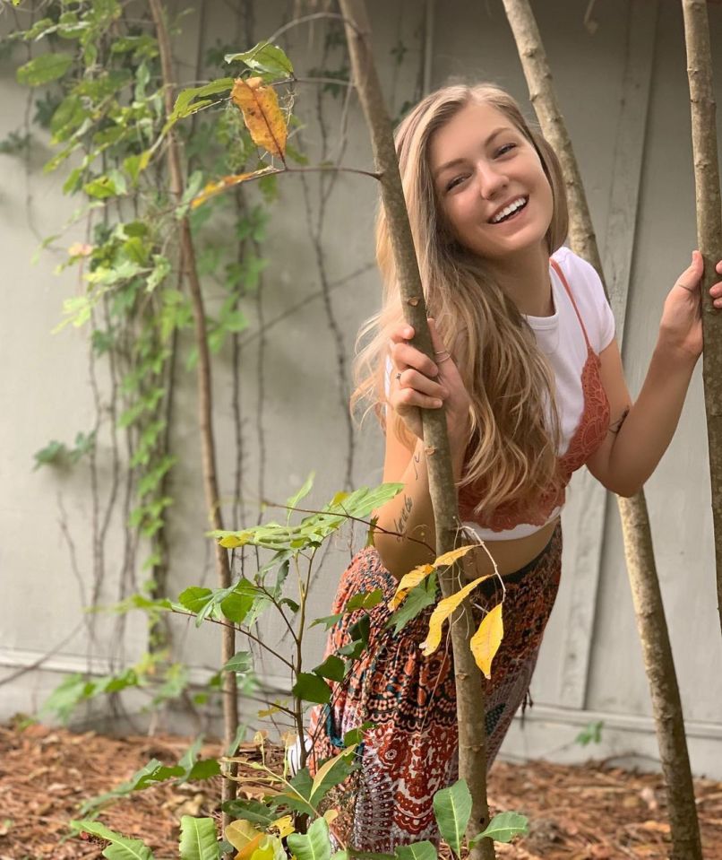 Woman smiling behind trees.