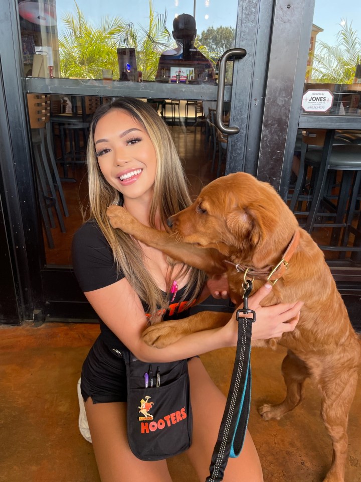 Woman in Hooters uniform hugging a golden retriever puppy.