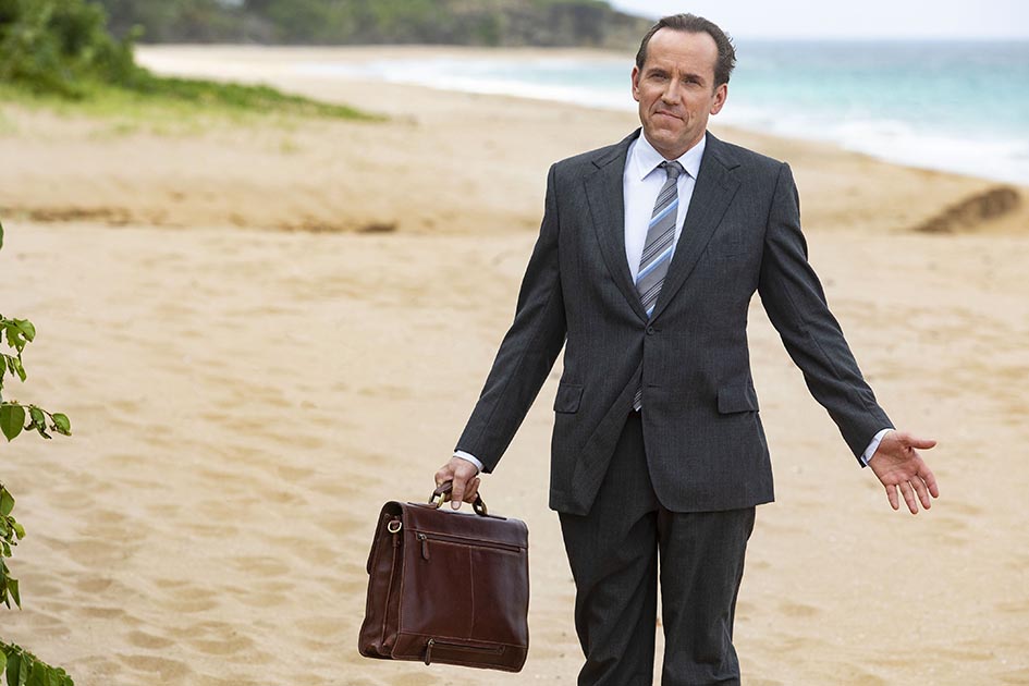 Ben Miller as DI Richard Poole on a beach, carrying a briefcase.