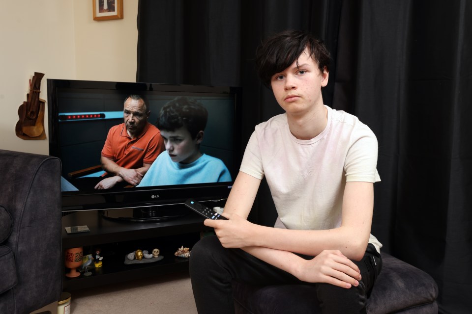 A teenager sits holding a TV remote, looking at the camera, with a Netflix drama playing on the television behind him.