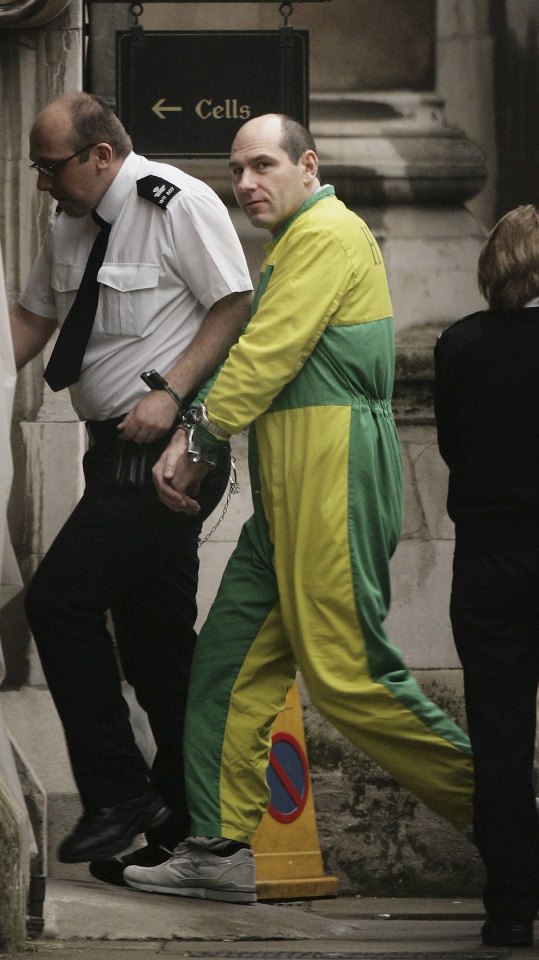A handcuffed man in a yellow and green jumpsuit is escorted by a police officer.