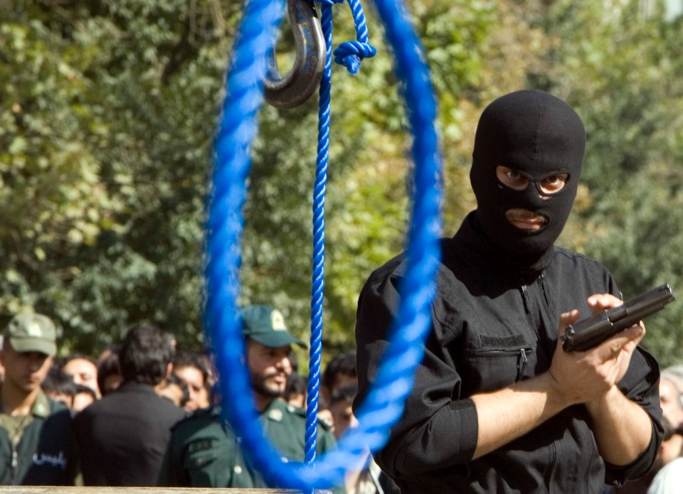 A masked Iranian policeman holds a gun before a public hanging.