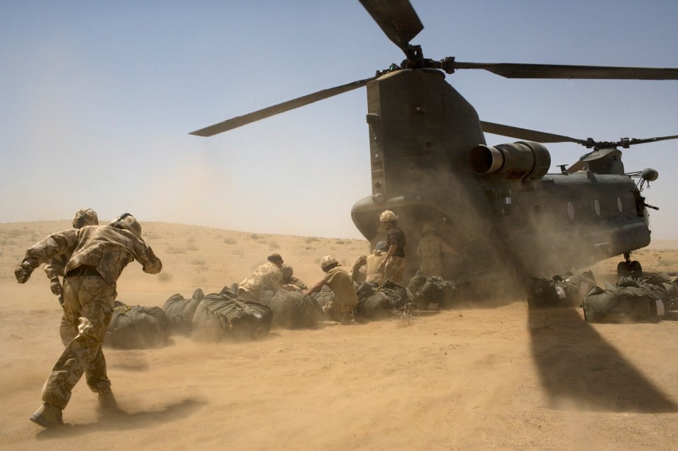British soldiers unloading supplies from a Chinook helicopter in a desert.
