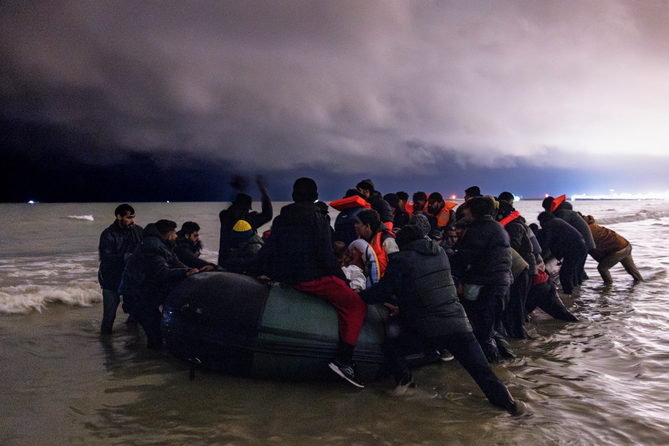 Migrants in an inflatable boat arriving on a beach at night.