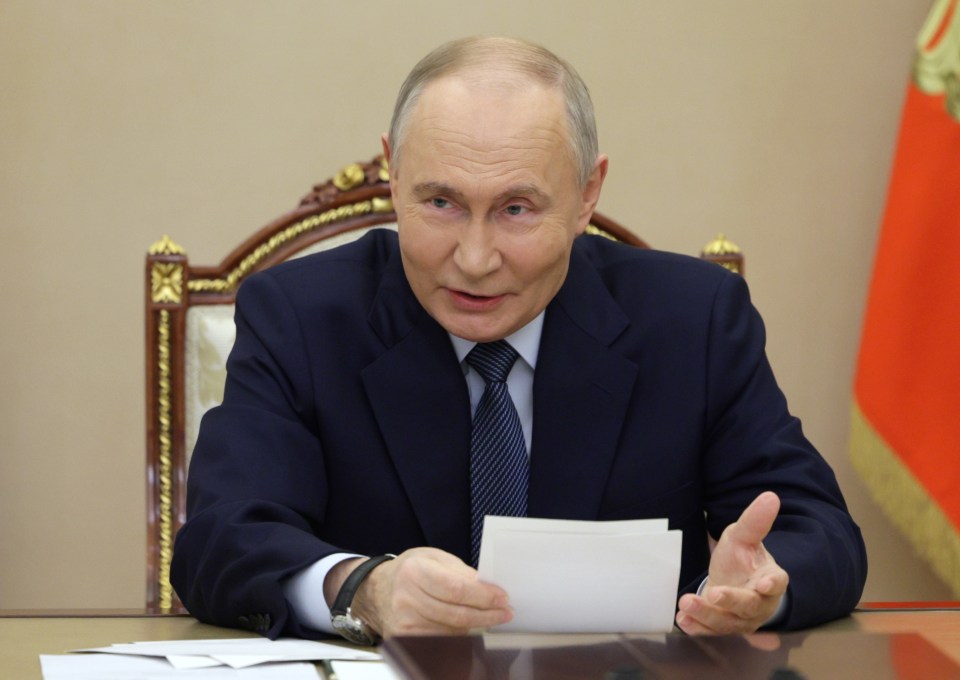Vladimir Putin at a meeting, reviewing documents.