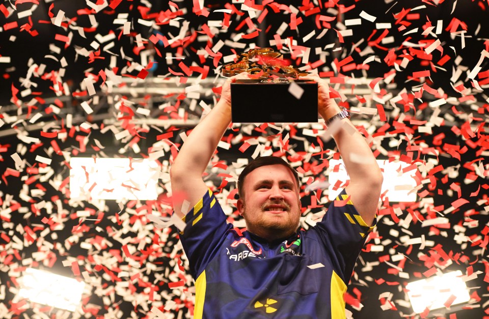A darts player holding up the Ladbrokes UK Open trophy amidst falling confetti.