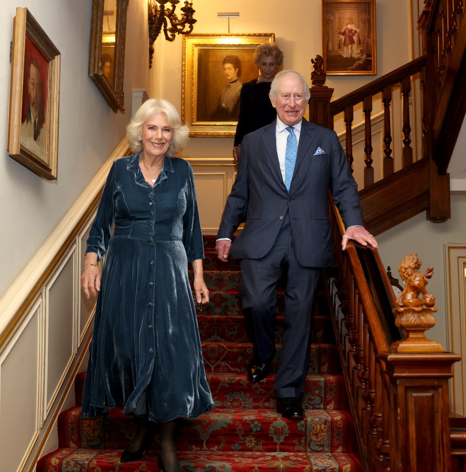 King Charles III and Queen Camilla descending a staircase.
