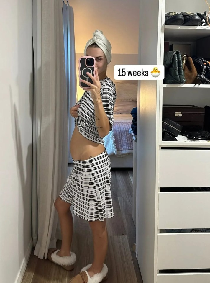 A pregnant woman at 15 weeks, taking a selfie of her baby bump.