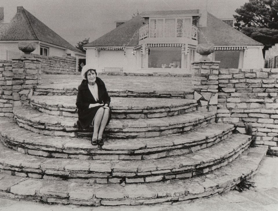 Black and white photo of Mimi Smith sitting on stone steps in front of her home.