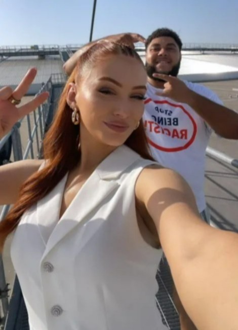 Woman in white vest and man in "Stop Being Racist" shirt on a rooftop.