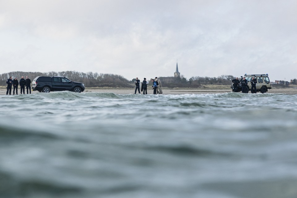 French police officers on a beach watching migrants board a boat.