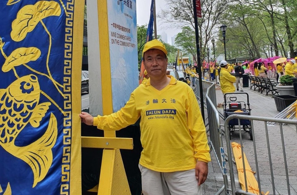 Man in yellow Falun Dafa shirt standing next to a parade banner.