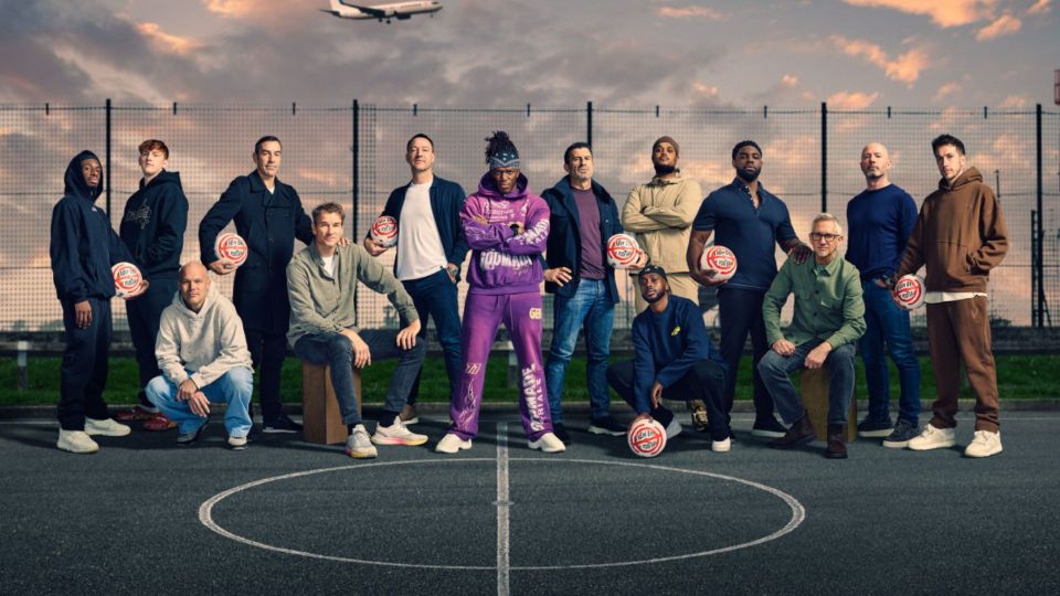Group of men posing on a basketball court, holding soccer balls.