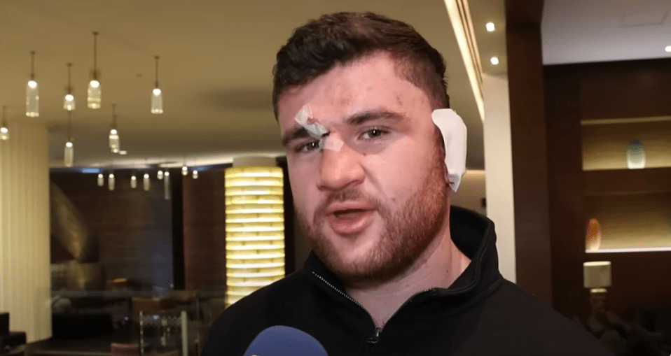 Man with facial bandages speaking to a microphone.