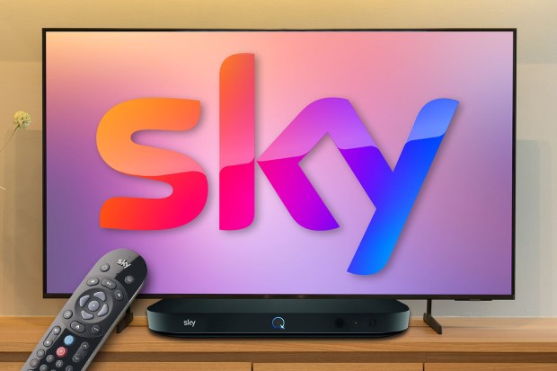 Sky Q box and remote on a shelf in front of a TV displaying the Sky logo.