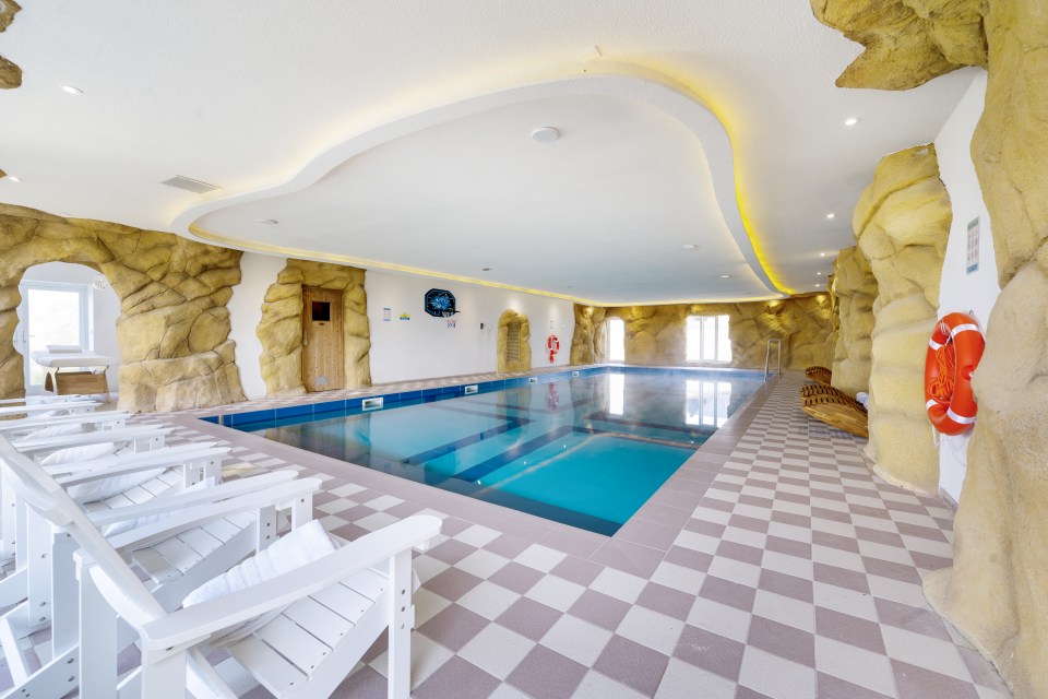 Indoor swimming pool with rock walls and white lounge chairs.