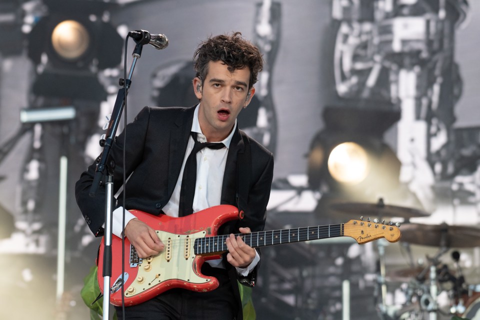 Matt Healy of The 1975 playing a red guitar on stage.