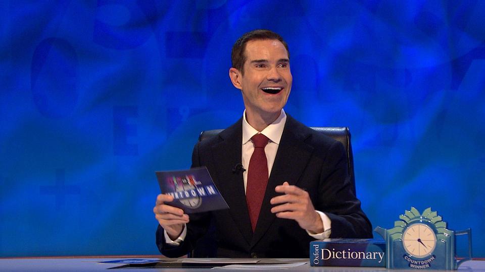 A man in a suit smiles and holds a Countdown game card.