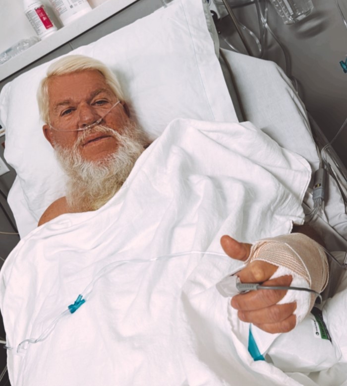 Man in hospital bed with bandage on hand.