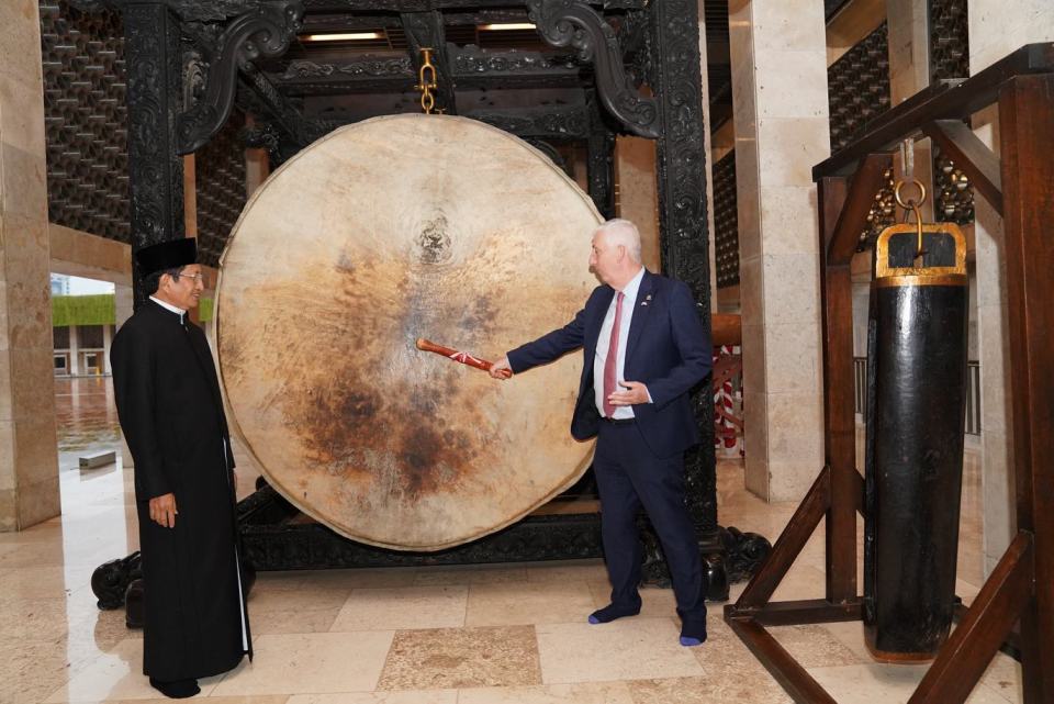 Two men standing near a large drum, one man holding a drumstick.