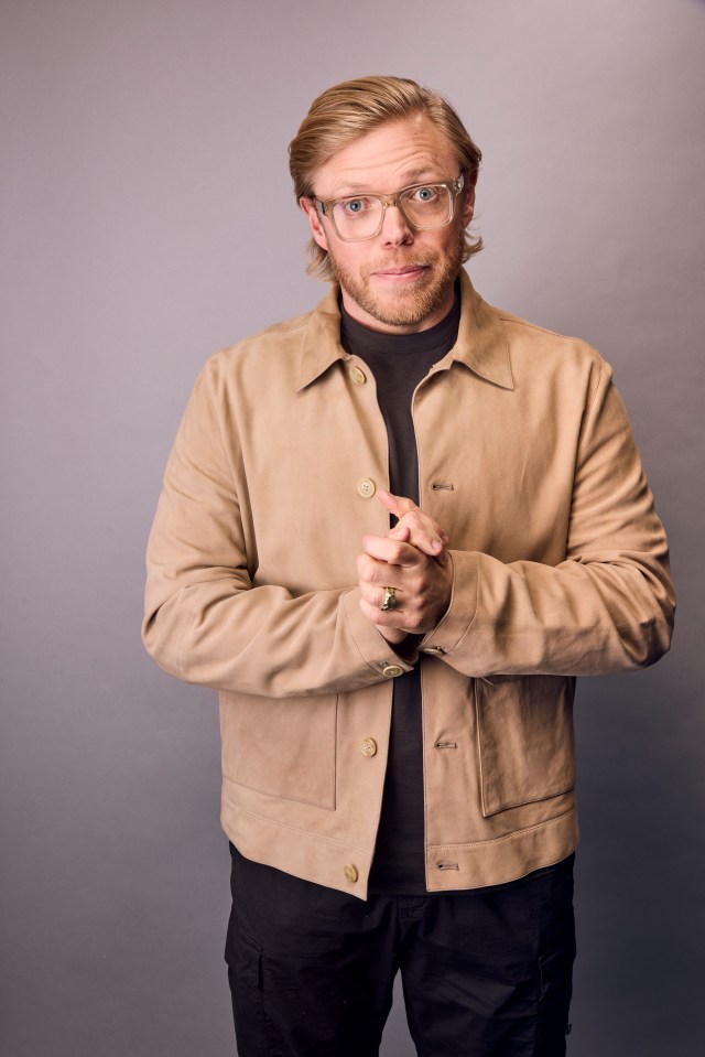 Portrait of a man wearing glasses and a tan jacket.