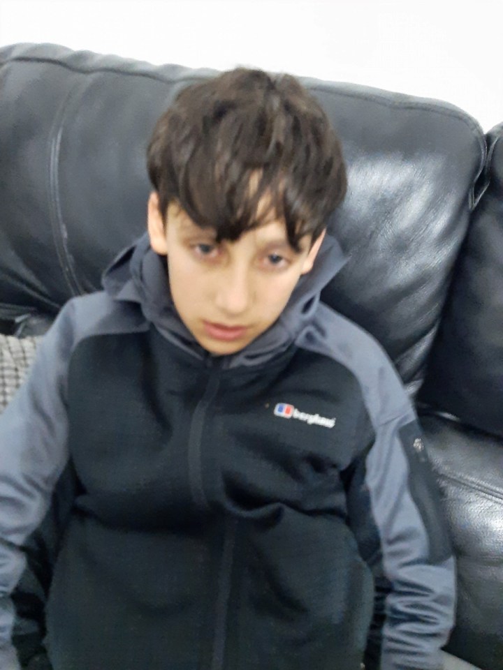 Boy in a gray and black zip-up jacket sitting on a couch.