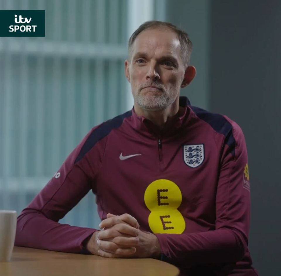 Man in England tracksuit sits at table.