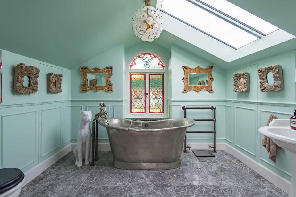 Elegant bathroom with a clawfoot tub, stained-glass window, and decorative mirrors.