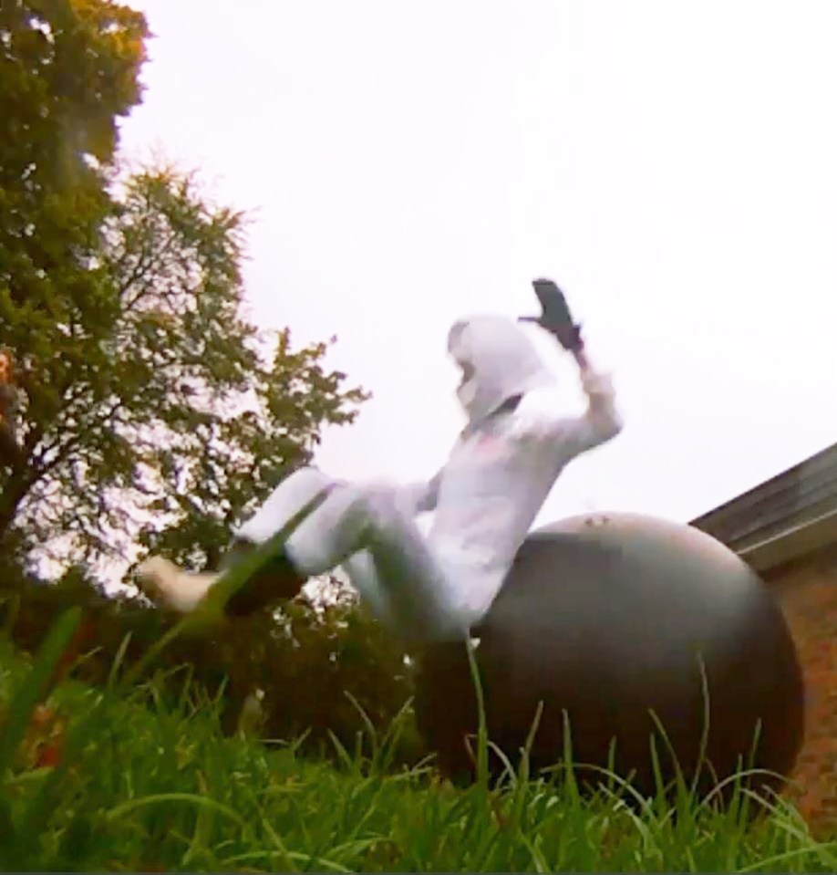 Person in white suit falling off a large ball in a grassy area.