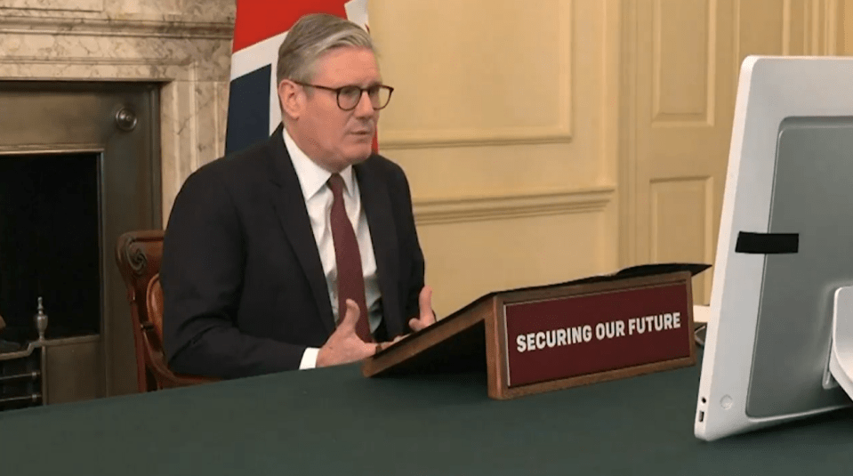 Screenshot of a man in a suit speaking during a video conference, with a sign reading "Securing Our Future."