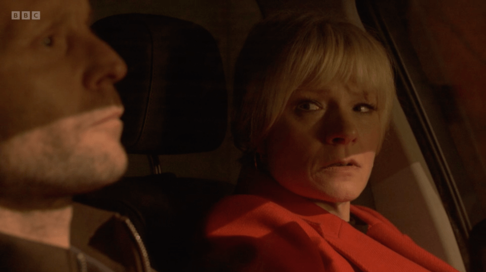 Screenshot of a woman in a red coat and a man sitting in a car.