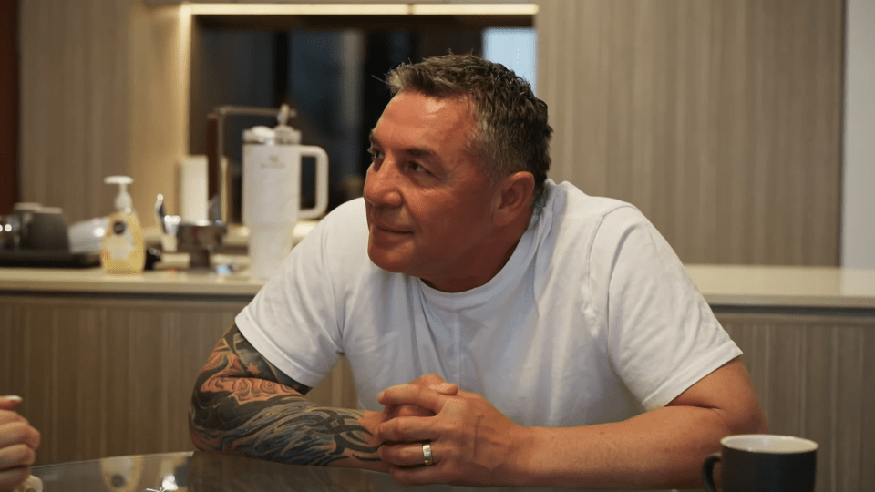 Man with tattoos sits at a table, looking off to the side.