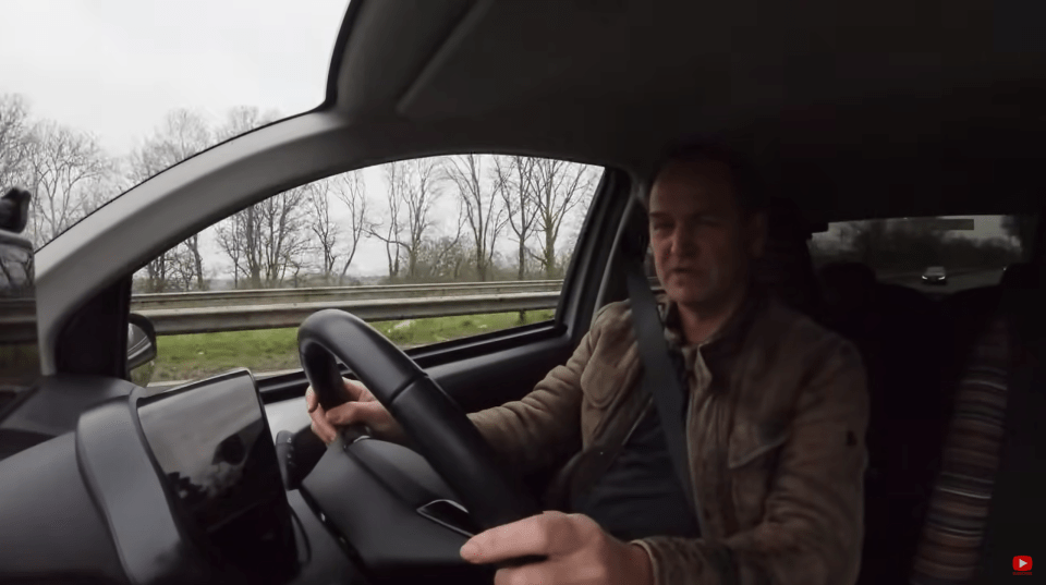 Screenshot of a man driving a car on a highway.