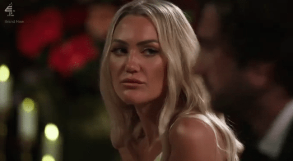 Screenshot of a blonde woman looking thoughtfully at someone out of focus.