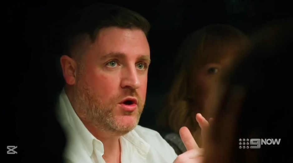Screenshot of a man speaking, with a woman in the background.