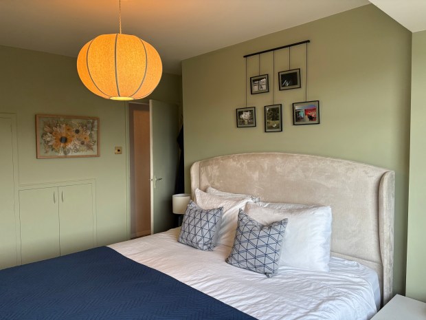 Bedroom with beige headboard, navy blue blanket, and framed photos.