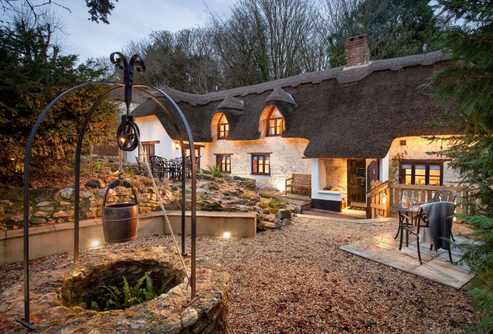 Thatched-roof cottage at dusk with well and patio seating.