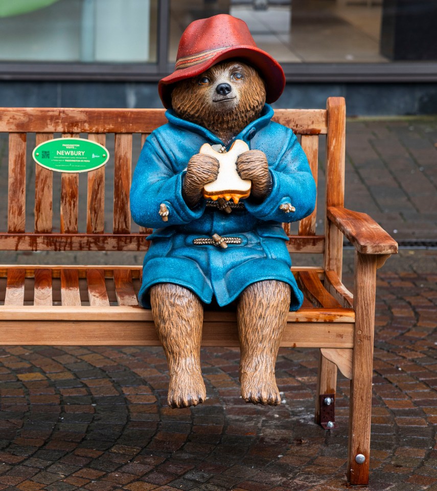 Statue of Paddington Bear sitting on a bench, eating a marmalade sandwich.