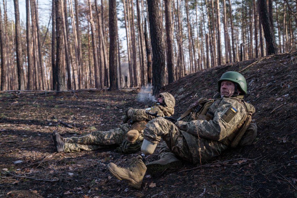 Two Ukrainian soldiers resting in a forest; one soldier has a prosthetic leg.