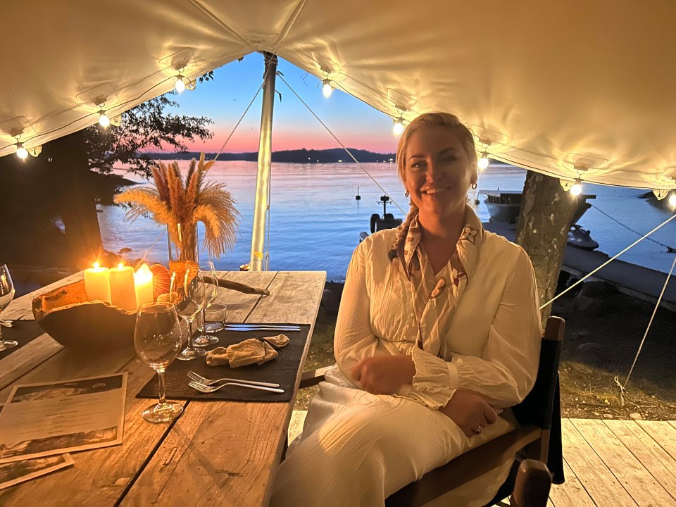Woman sitting at a table outdoors at sunset, enjoying a meal.