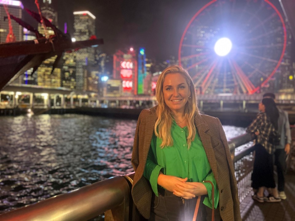Woman in a green shirt and brown jacket in Hong Kong at night.