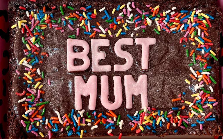Chocolate brownie with "Best Mum" in pink icing and rainbow sprinkles.
