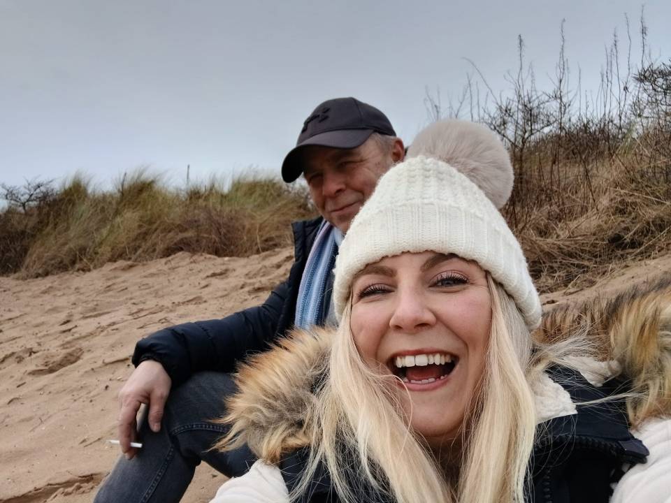 A smiling woman and man sitting on a sandy beach.