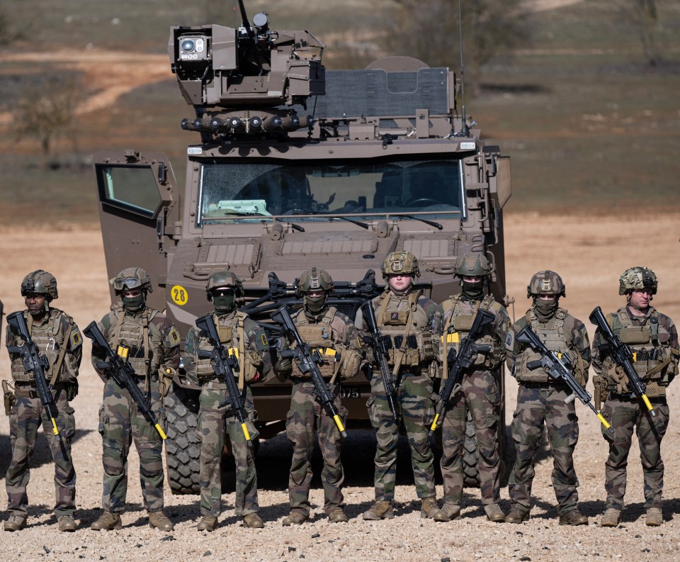 French soldiers standing in formation with their weapons in front of military vehicles.