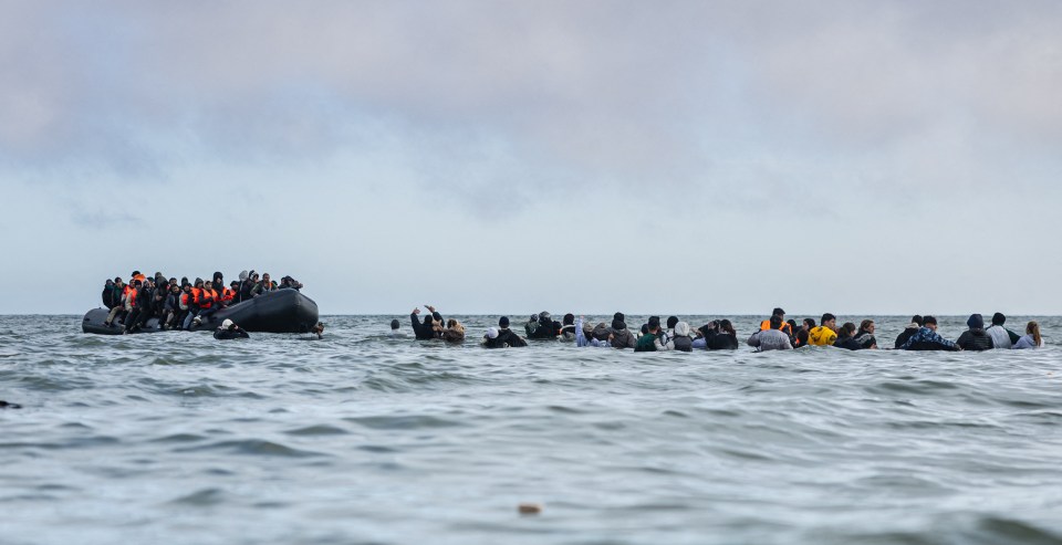 Migrants in a small boat and in the water attempting to cross the English Channel.