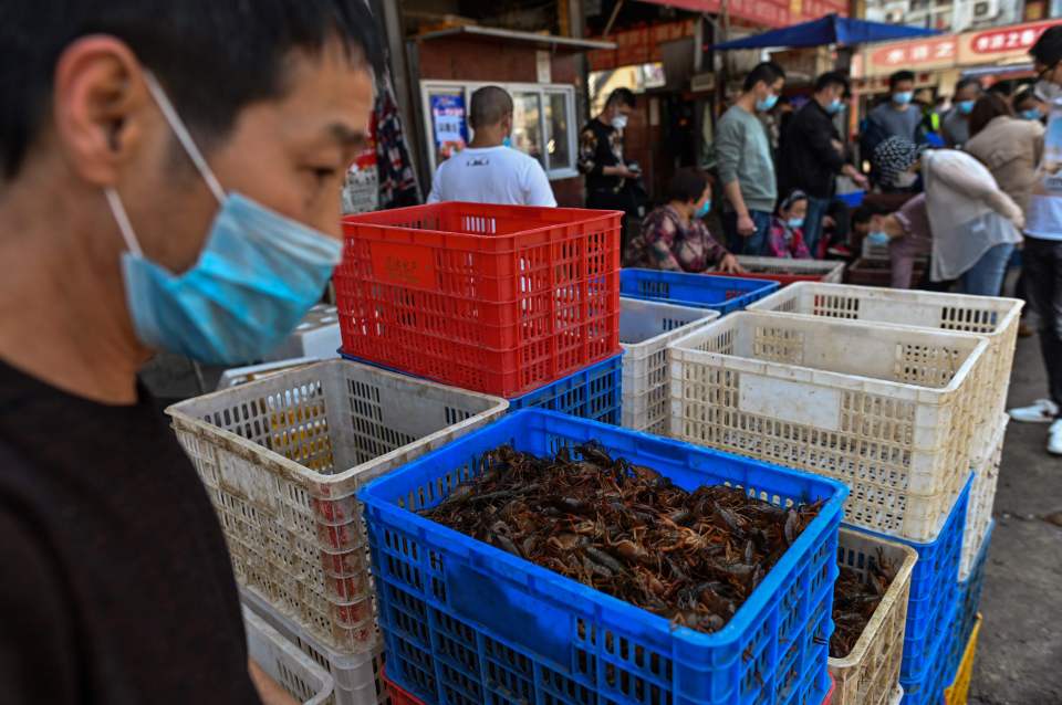 A person wearing a face mask at a market where live crayfish are sold in plastic crates.
