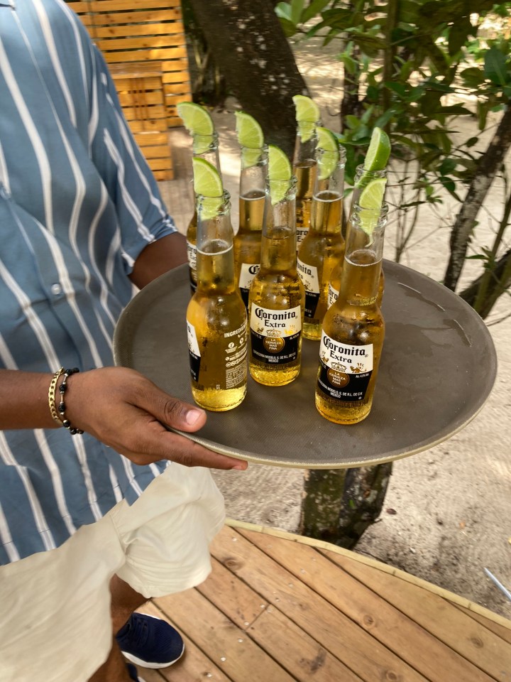 Person carrying tray of Corona Extra beers with lime wedges.